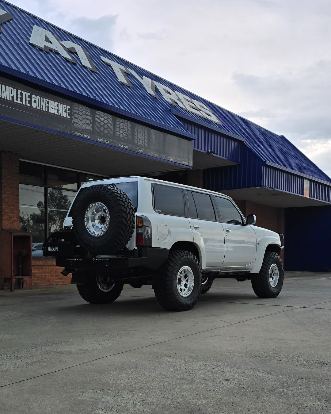 White lifted SUV parked outside a building with a blue metal roof
