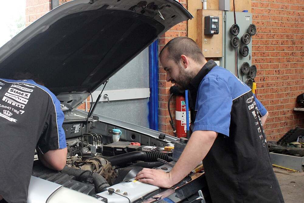 Two Mechanics Working Under an Open Car Hood in A Garage — Bay City A1 Tyres in North Geelong, VIC