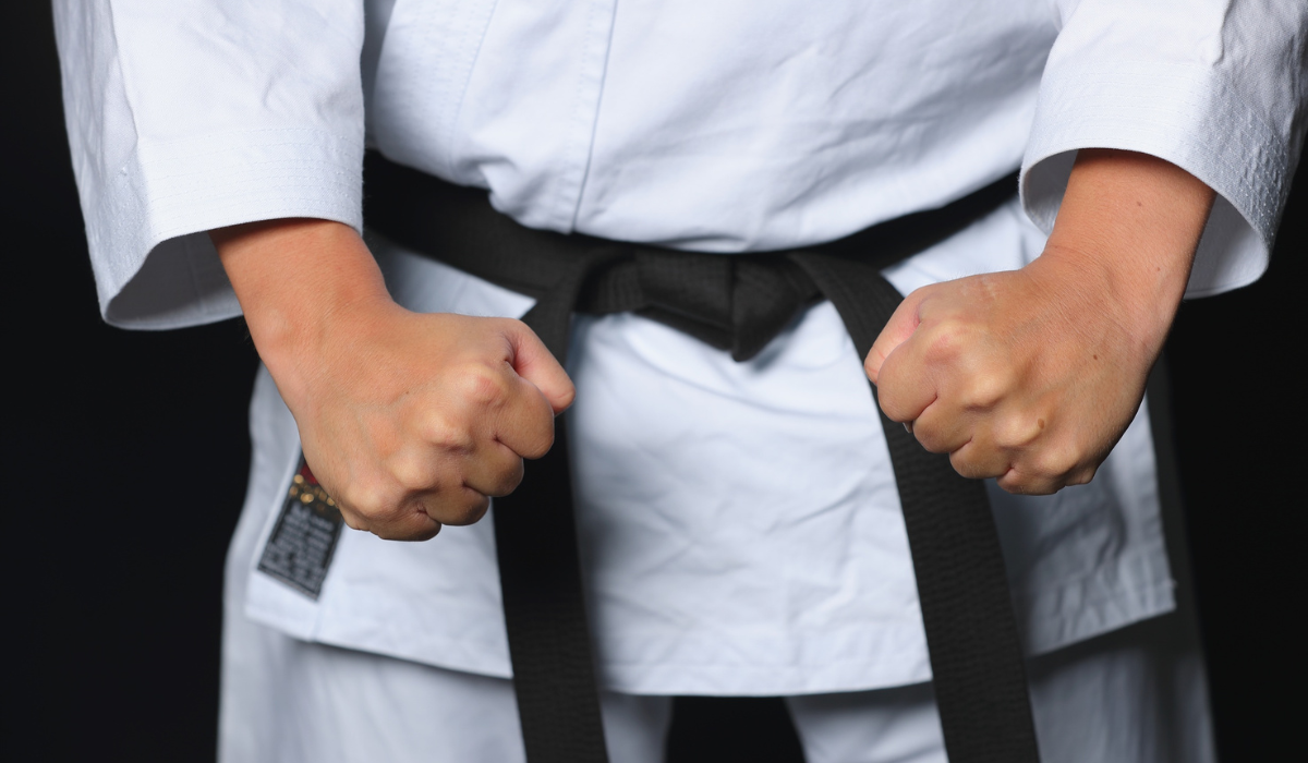 Person in a white martial arts uniform holding a black belt at the waist