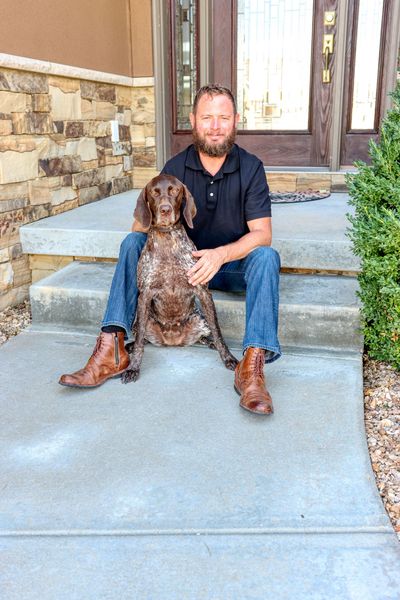 A man is sitting on the steps of a house with a dog. Independence Built Custom Home Builder in Nebraska