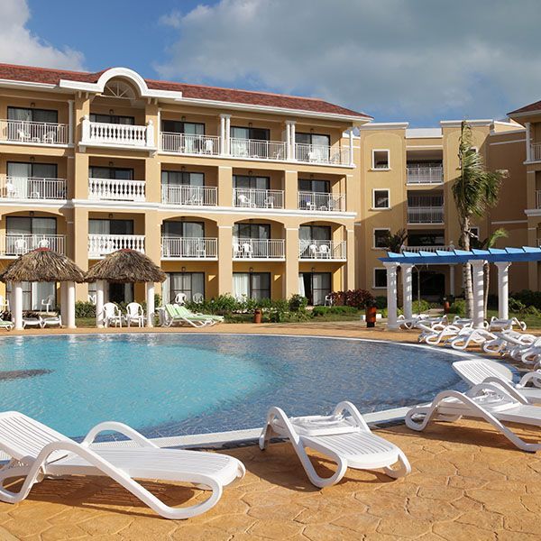 Resort hotel with balconies beside a curving pool and white lounge chairs under a blue sky
