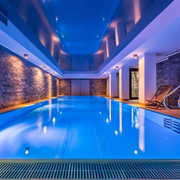 Indoor pool with blue lighting, stone walls, and lounge chairs beside the water
