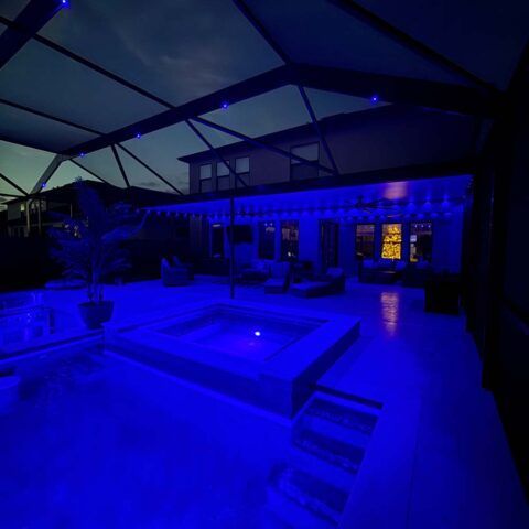 Blue-lit backyard patio with a covered seating area and a square fire pit at night