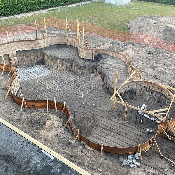 Curved concrete foundation under construction with wooden forms and rebar in a grassy lot
