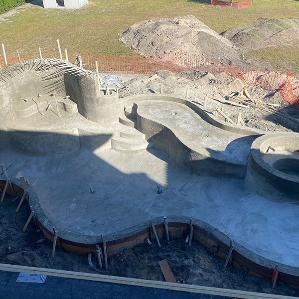 Concrete pool under construction with curved ramps, rebar, and dirt piles around it