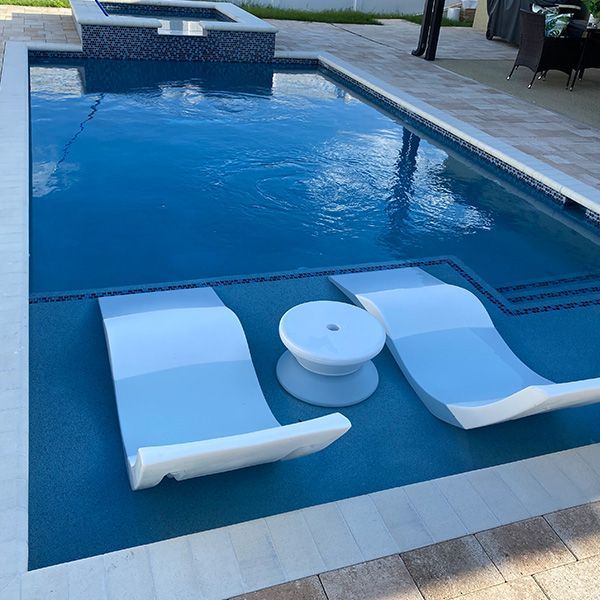 Two white lounge chairs in shallow blue pool water beside a pool deck