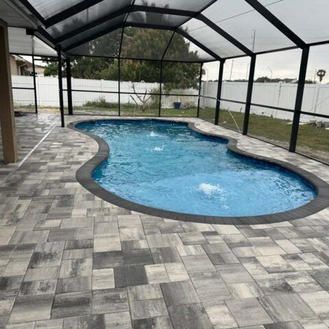 Covered backyard pool with blue water and gray paver deck, enclosed by a screened patio