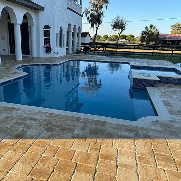Backyard swimming pool beside a white house with arched windows and a patio, under clear blue sky