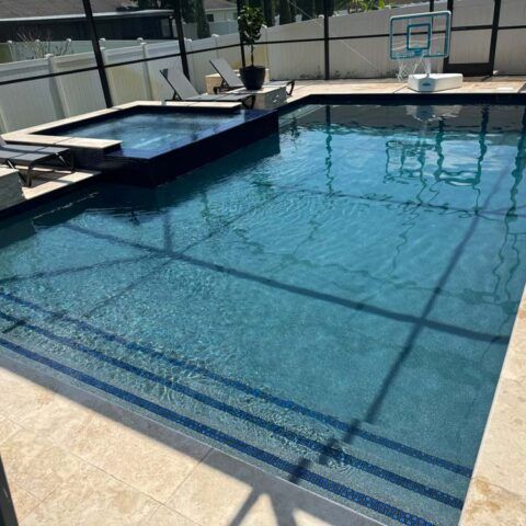 Backyard swimming pool with attached spa, beige deck, and basketball hoop on the far side