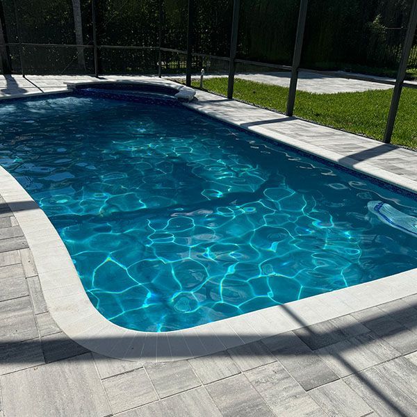 Backyard swimming pool with clear blue water, white stone deck, and black safety fence