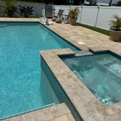 Backyard pool with turquoise water and a raised hot tub beside a tan stone deck