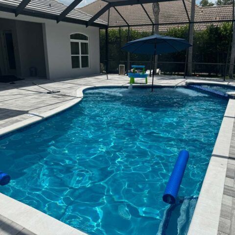 Backyard swimming pool with a blue float, patio cover, and clear blue water in bright sunlight