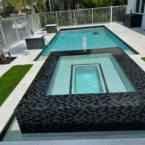 Modern backyard pool with a raised square hot tub and turquoise water, surrounded by white fencing and stone decking
