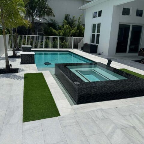 Modern backyard with a swimming pool, raised hot tub, and white patio beside a white house