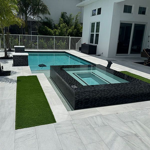 Modern backyard with turquoise pool, square hot tub, white patio, and white house with large glass doors