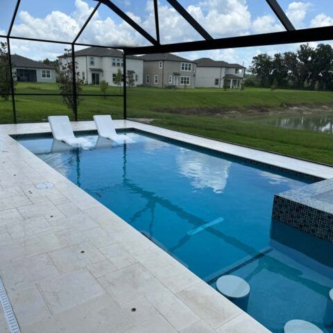 Outdoor pool with two white lounge chairs, screened enclosure, and grassy yard with houses in the background