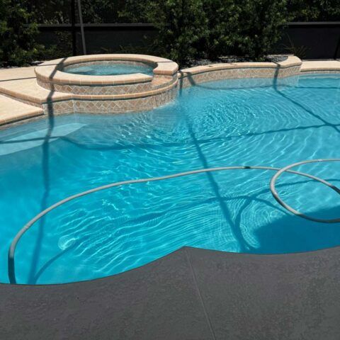 Backyard swimming pool with bright blue water, stone spa, and a hose floating across the surface