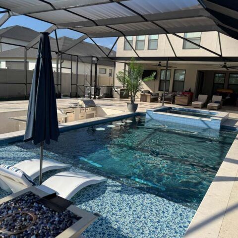 Covered backyard pool with hot tub, lounge chairs, and a patio in bright sunlight