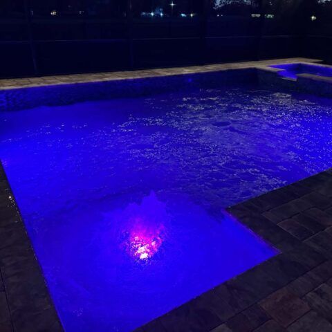 Blue-lit swimming pool at night with shimmering water and tiled deck