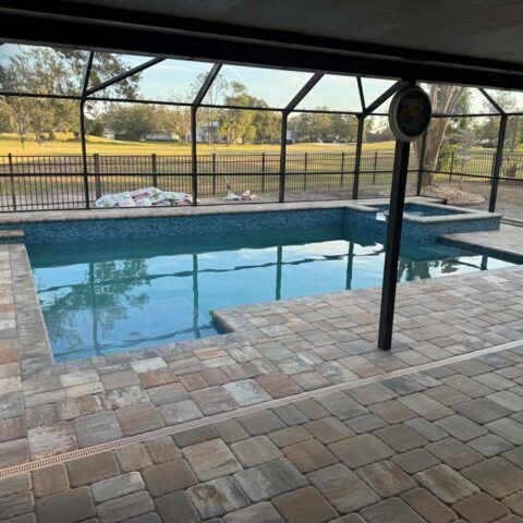 Covered backyard pool with brick patio and screened enclosure overlooking a grassy field