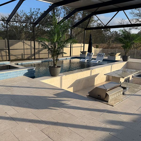 Backyard pool with beige pavers, lounge chairs, and a screened enclosure in bright sunlight