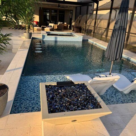 Modern patio with a rectangular pool, lounge chairs, and a square fire pit at sunset