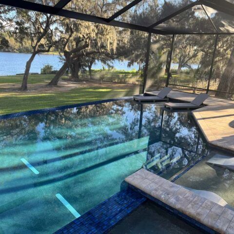 Backyard pool with a lake view, shaded patio, and large trees in the background