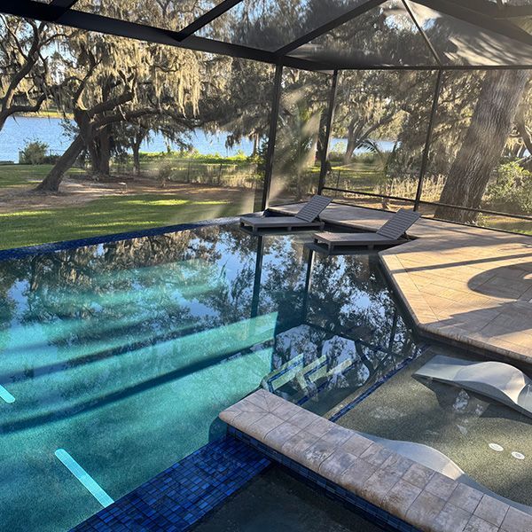 Screened pool with blue water, lounge chairs, and trees beyond the patio.