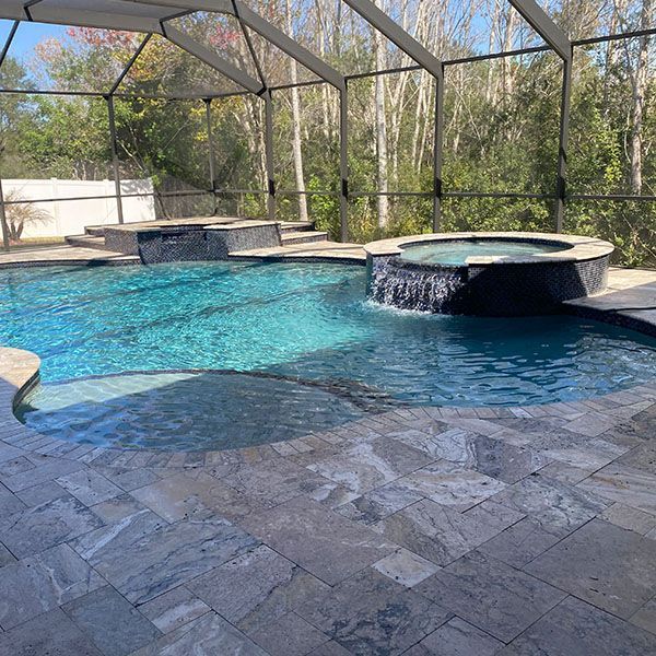 Backyard pool with blue water, hot tub, screened enclosure, and stone patio surrounded by trees