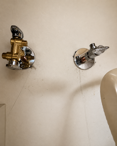 Two shiny wall fixtures on a beige wall, one brass-colored and one silver-colored.