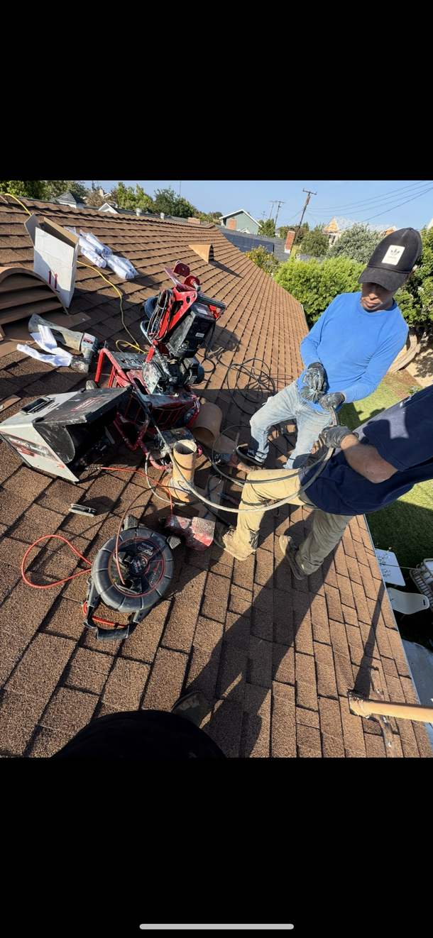 Person working outdoors with a red power tool near a house and garden bed