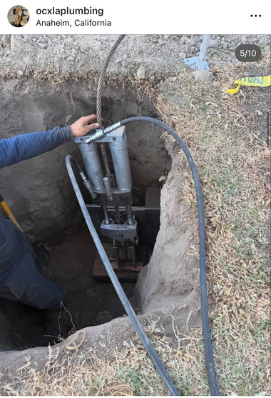 Three white pipes in a trench beside a wall, with soil mounds and a green hose connection at the top
