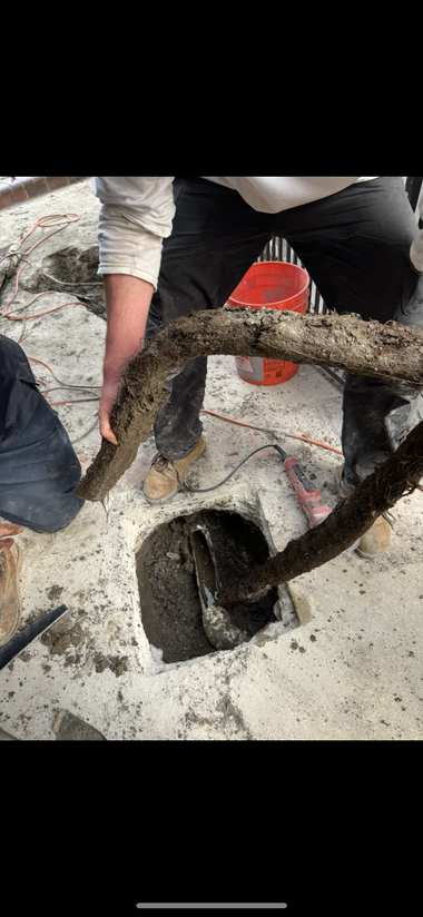 Worker uses a vacuum hose to clear mud from a narrow hole beside a concrete wall.