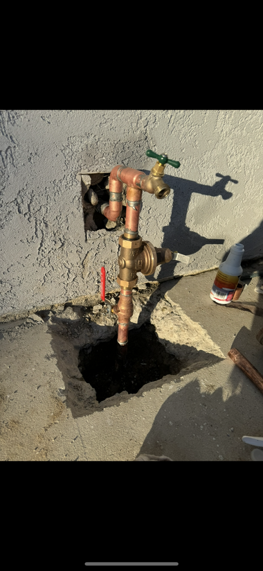 Hand turning a green faucet on a beige stucco wall, with plant leaves beside it.