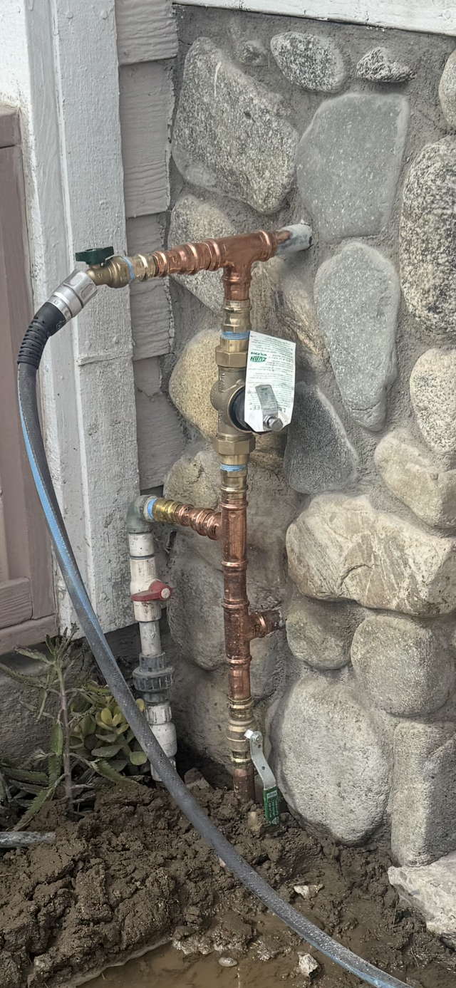 Open roadside water pipe with leaking fittings over a hole in asphalt