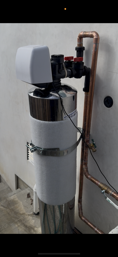 Close-up of rooftop edge with red tiles, copper piping, gray box, and green hose on stucco wall.