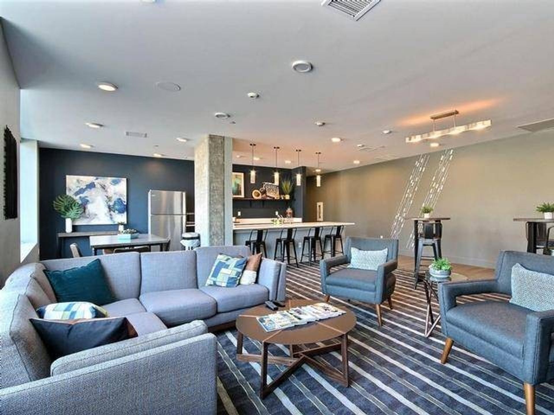 Modern lounge area with gray sectional, armchairs, kitchen island, and bar seating.