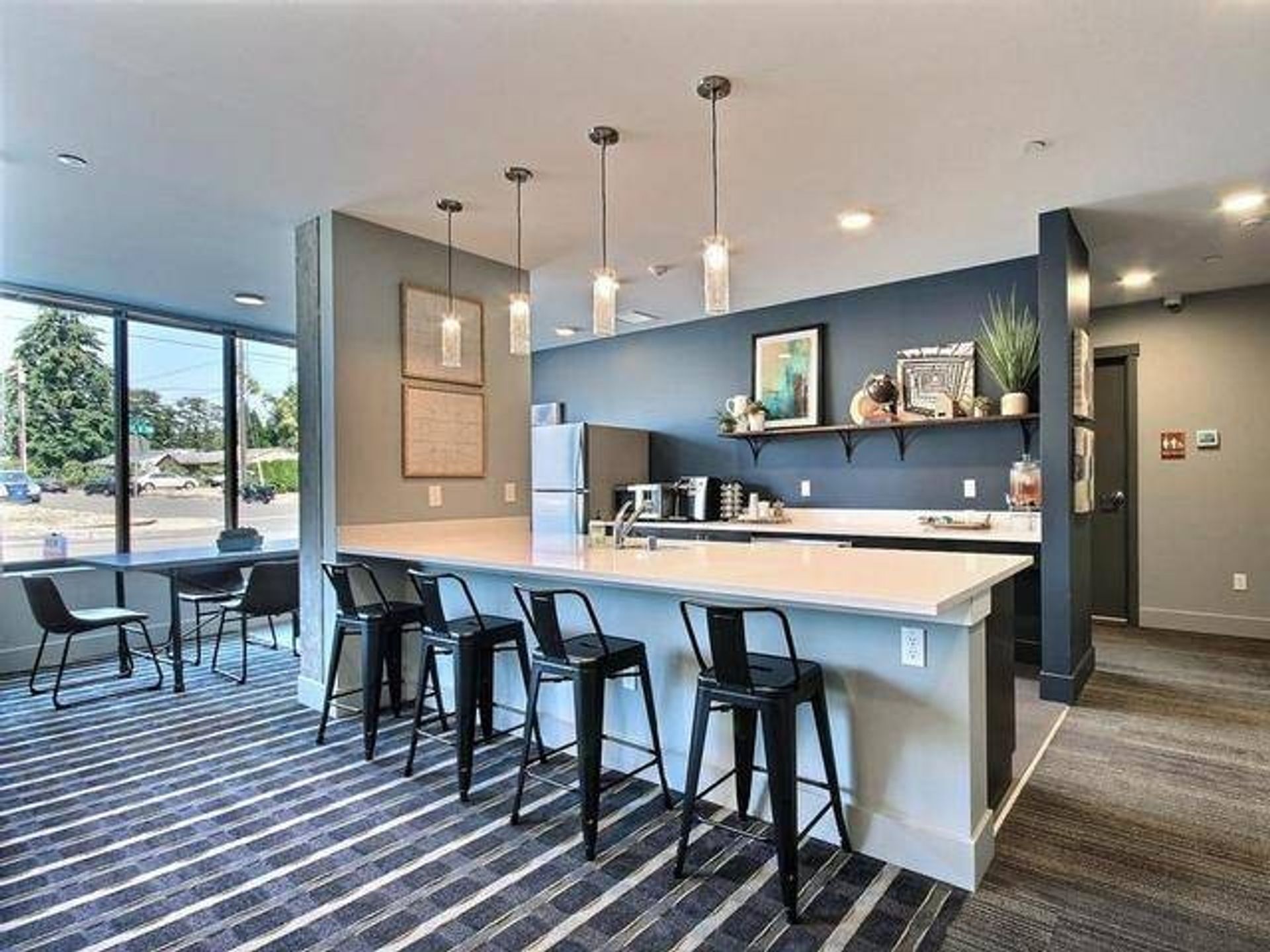 Modern kitchen with white countertop, black bar stools, and pendant lights.