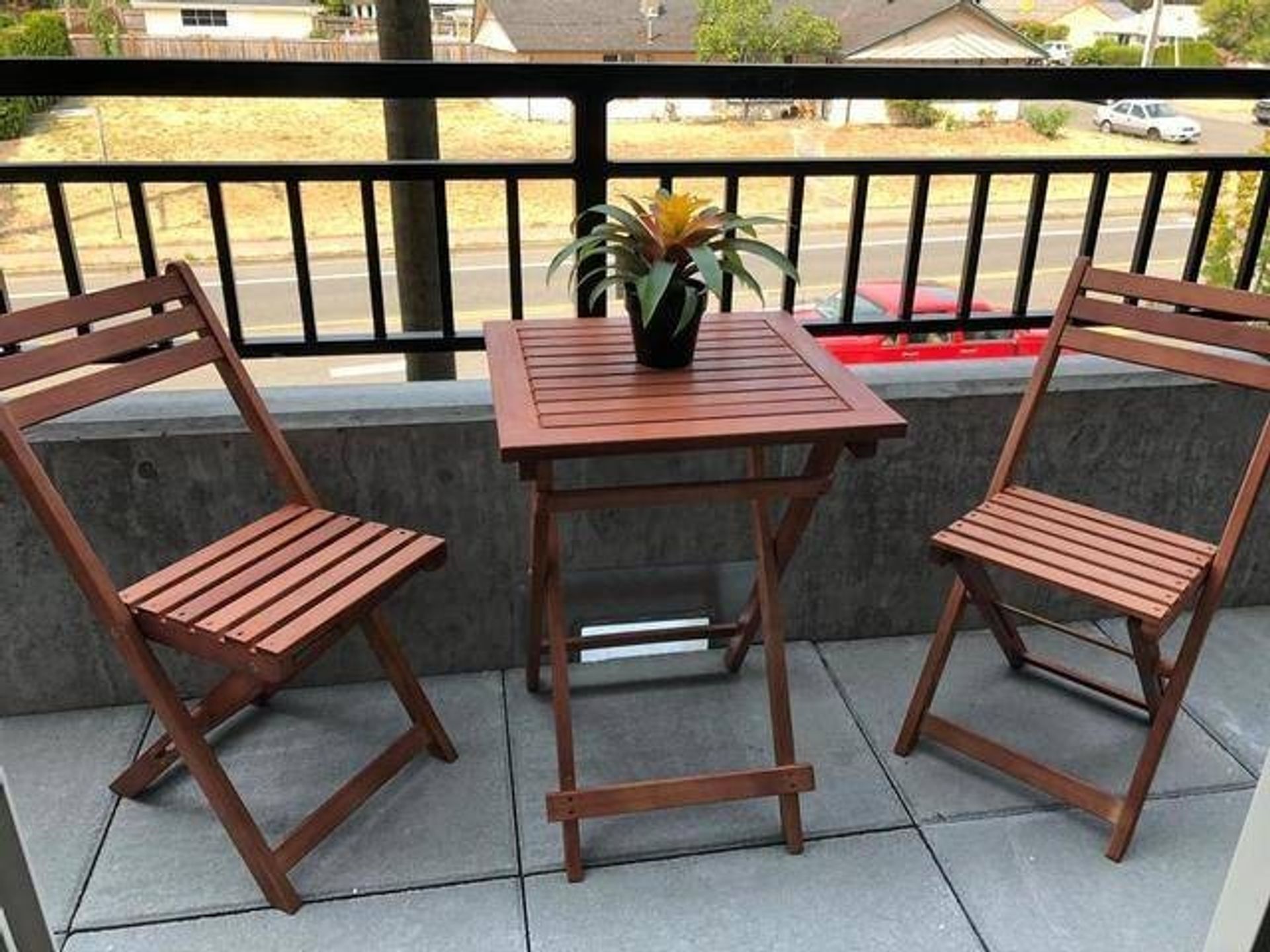 Wooden patio table and chairs with a potted plant on a balcony.