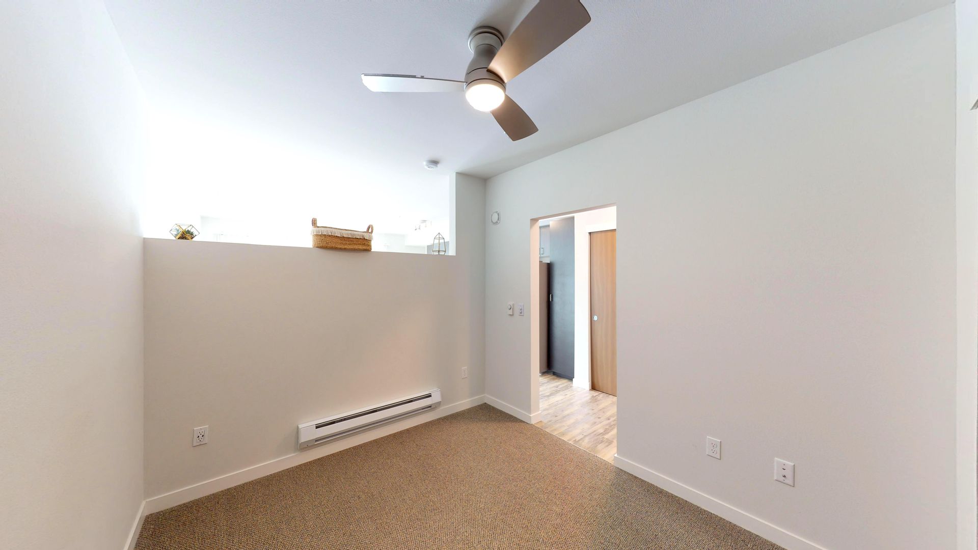 Empty room with beige carpet, white walls, and a ceiling fan; doorway leads to another room.