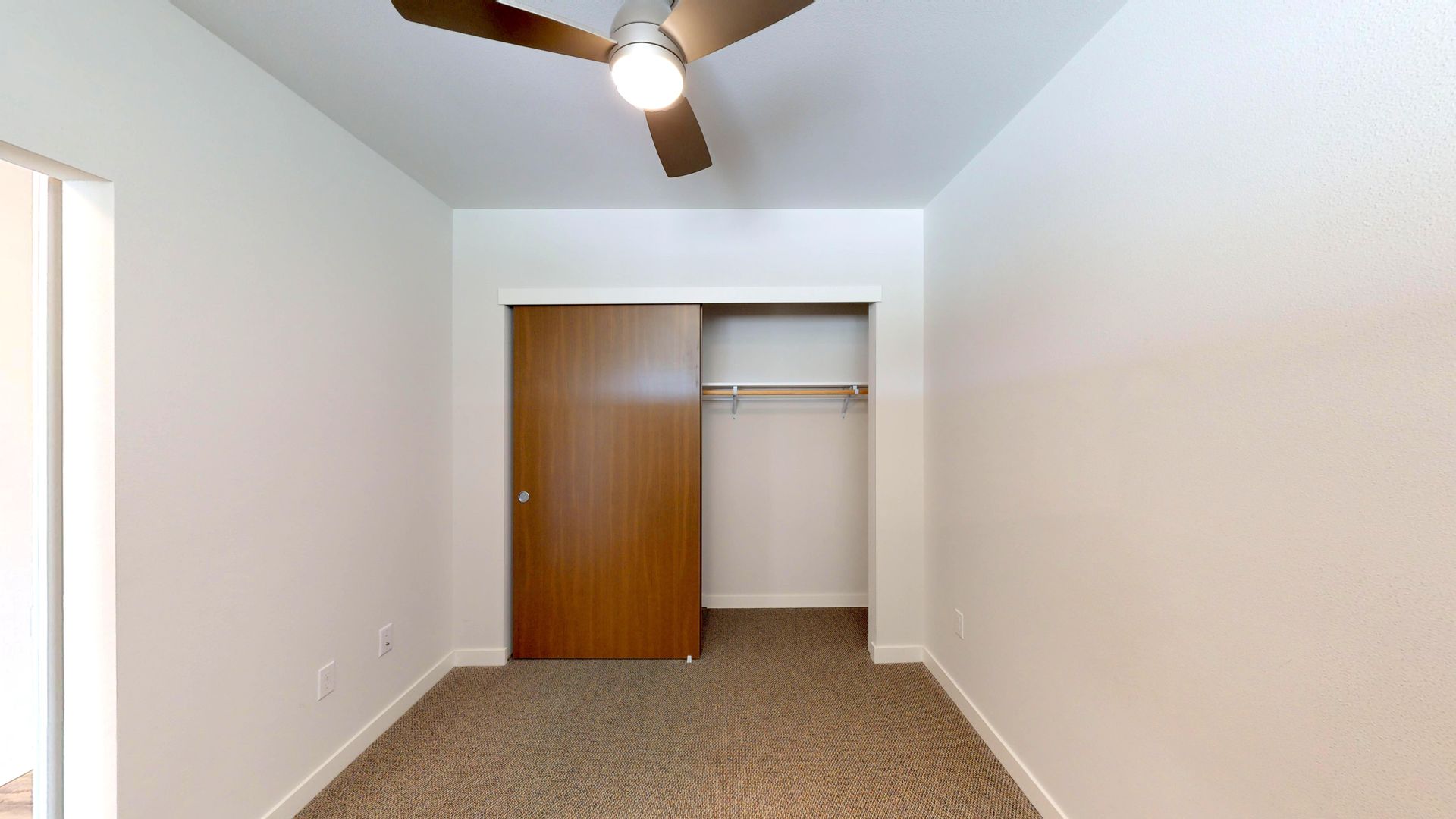 Empty bedroom with brown carpet, closet, and ceiling fan.