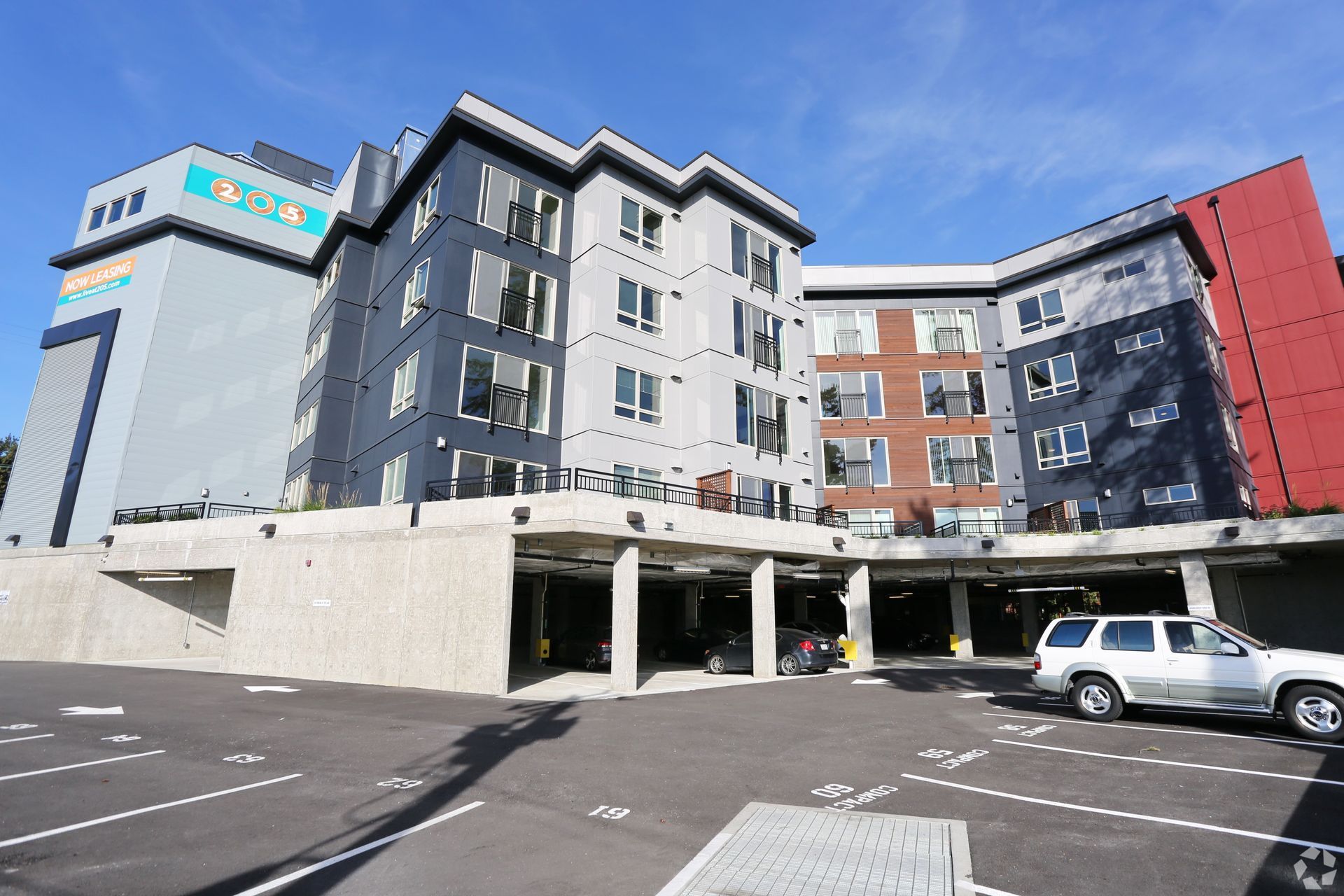 Apartment building exterior with a parking garage; gray, black, red exterior, blue sky, parked car.