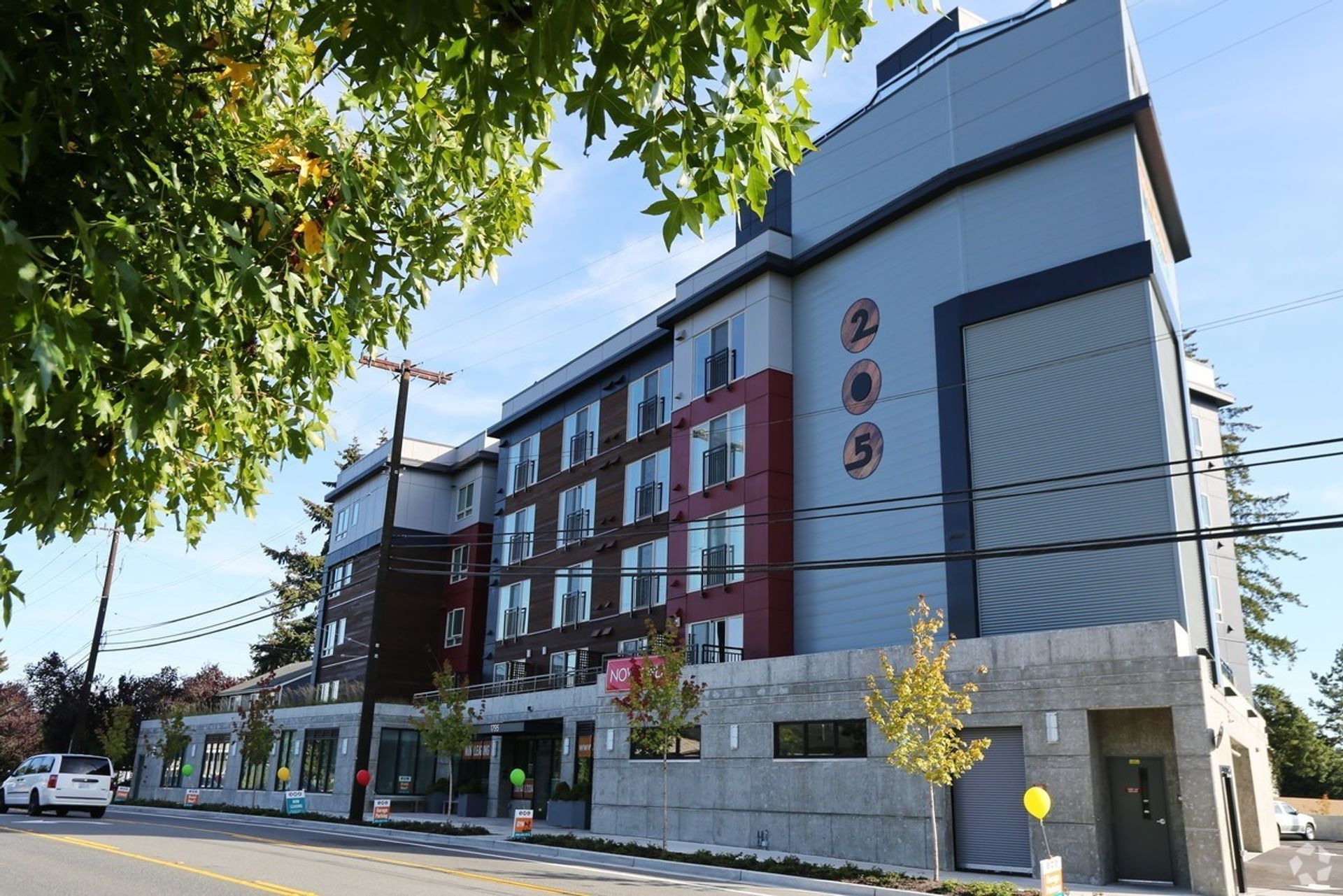 Multi-story apartment building with varying colors, a blue sky, and tree branches.