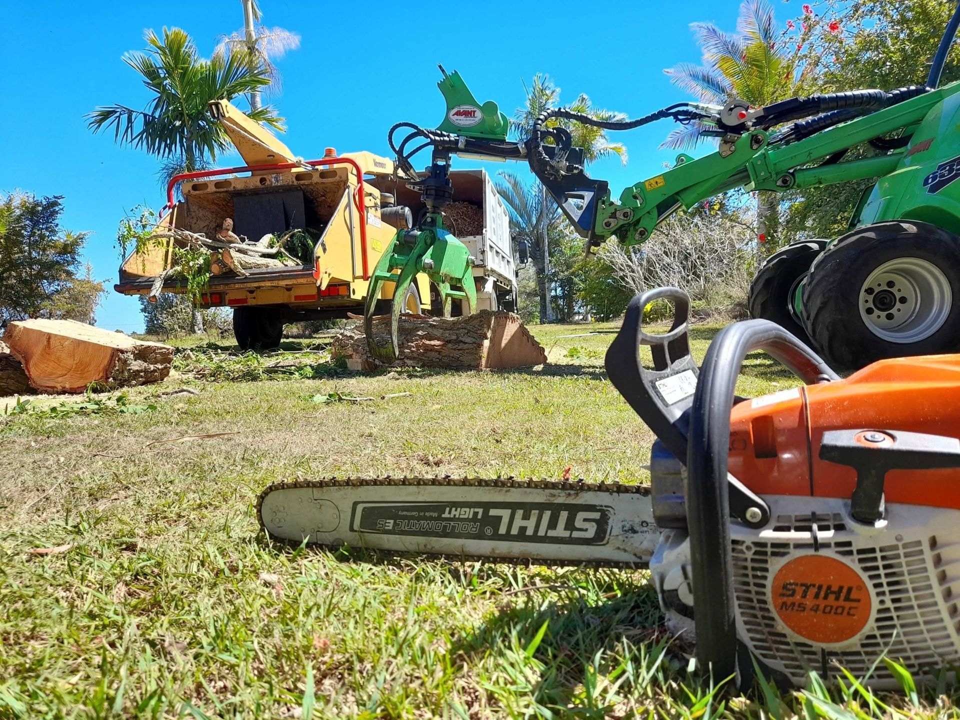 Workers in orange safety gear in a cherry picker cutting a tree branch outdoors