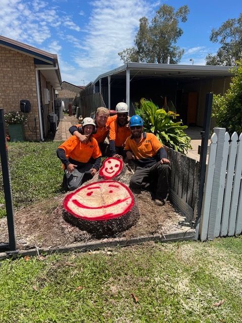 Workers in orange safety gear in a cherry picker cutting a tree branch outdoors
