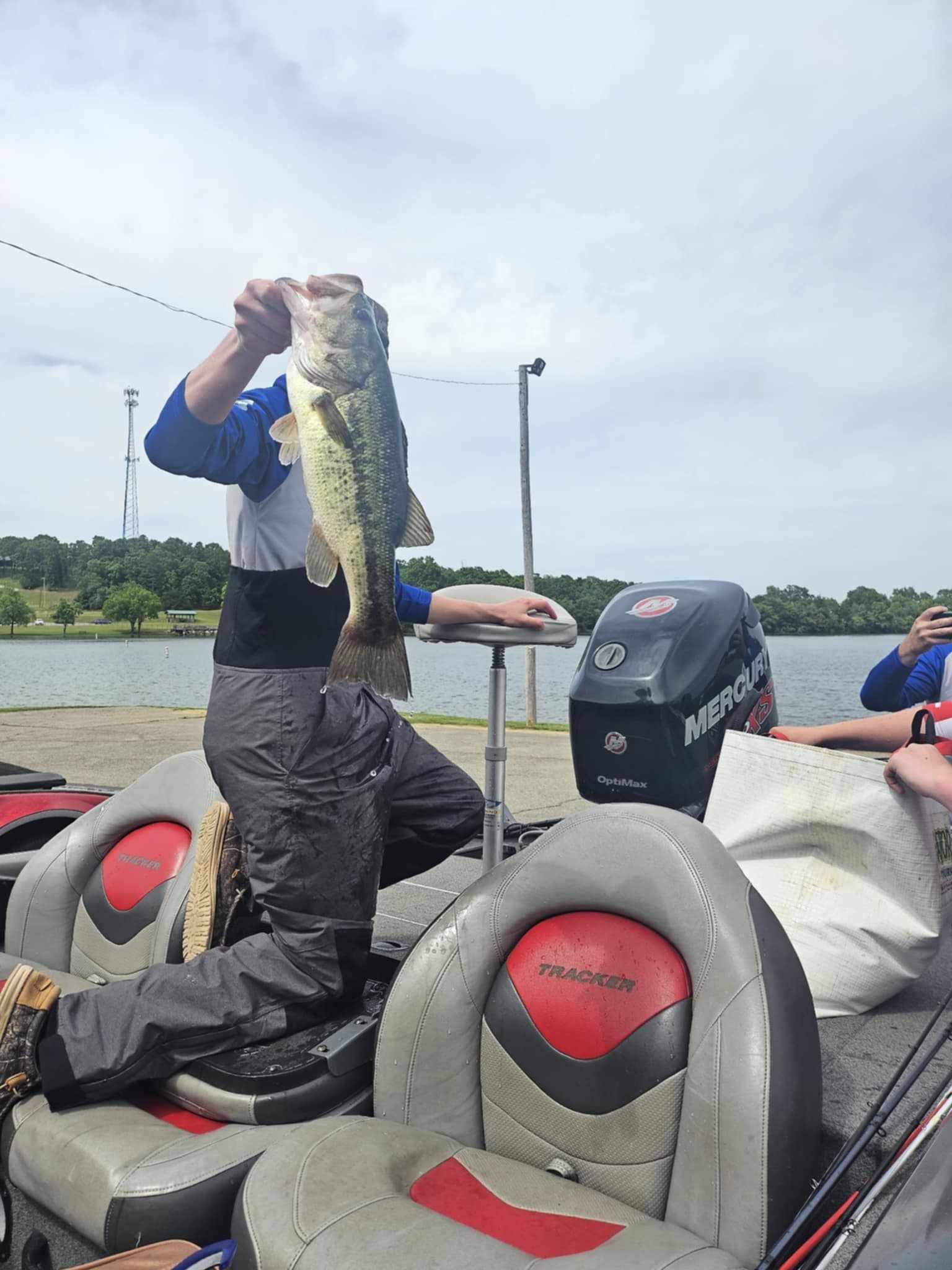 Angler on a boat holds up a large fish on a lake, with seats and a motor visible.