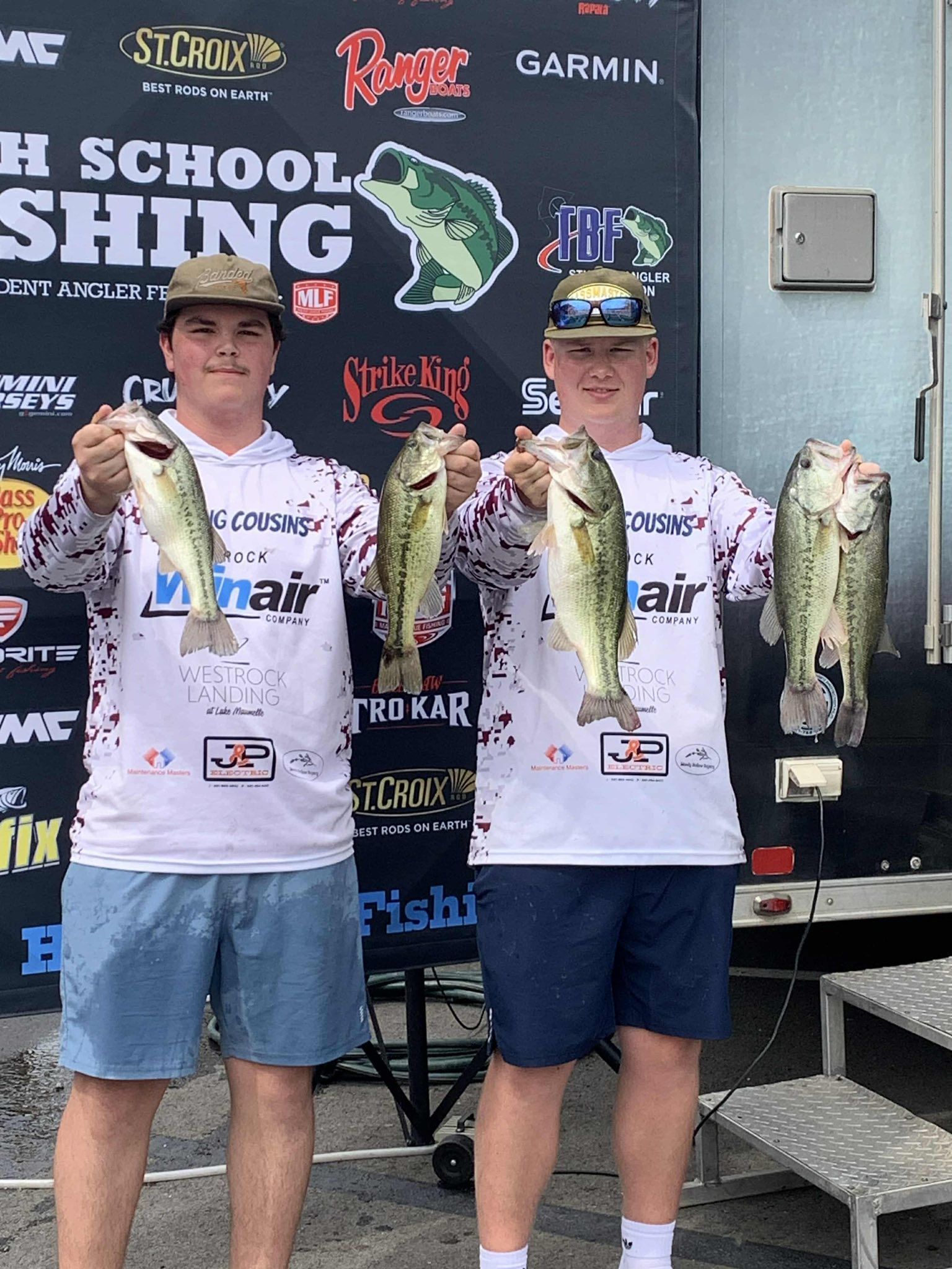 Two anglers holding four large fish onstage at a school fishing tournament awards event.