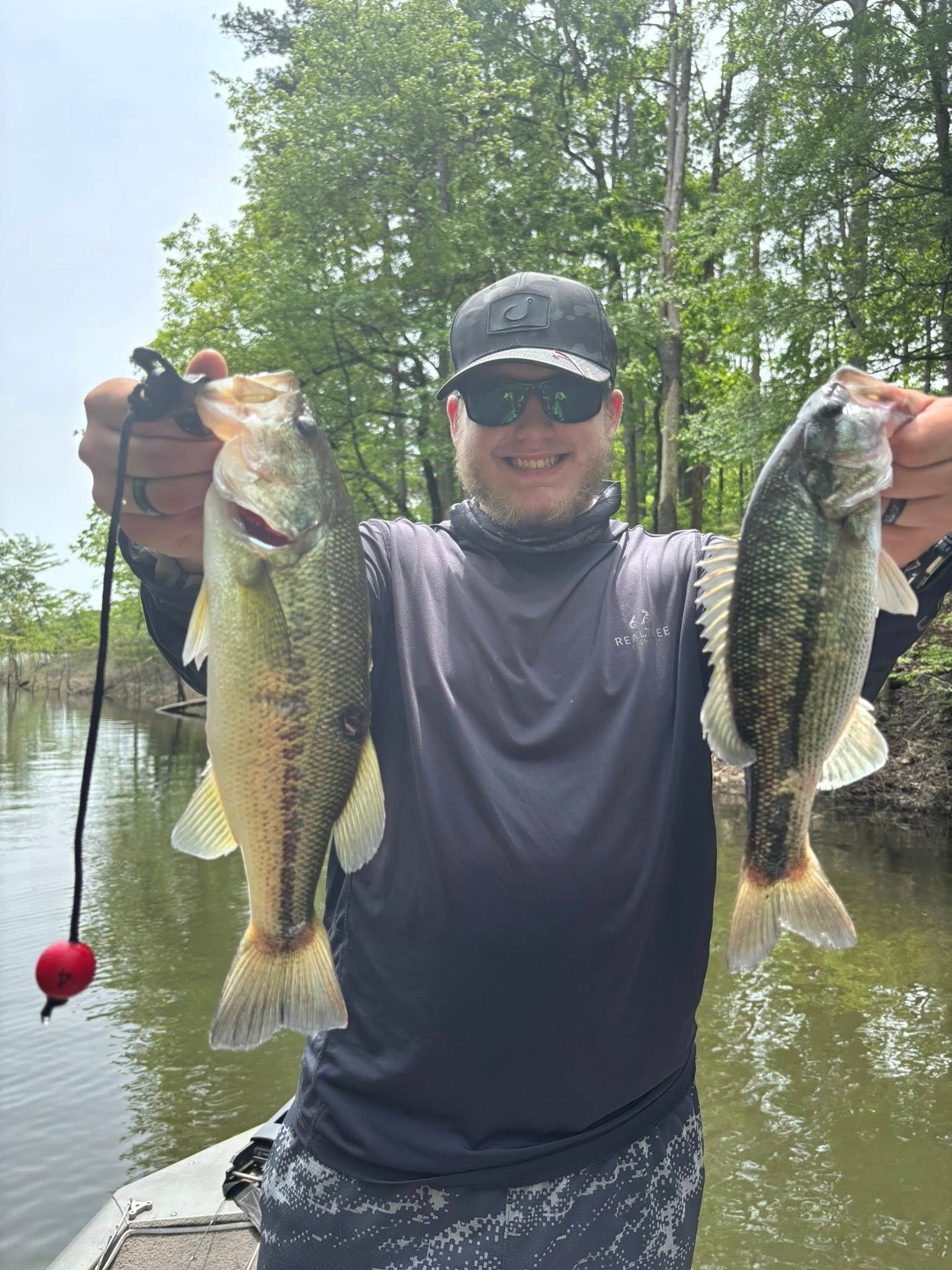 Man holding two large fish by a calm lakeside, with trees and water in the background
