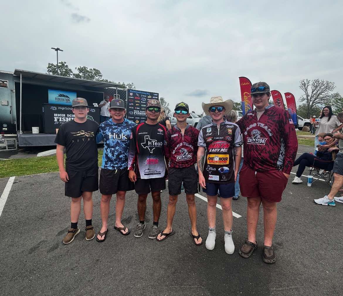 Group of six cyclists posing in front of a truck at an outdoor event, wearing team jerseys.