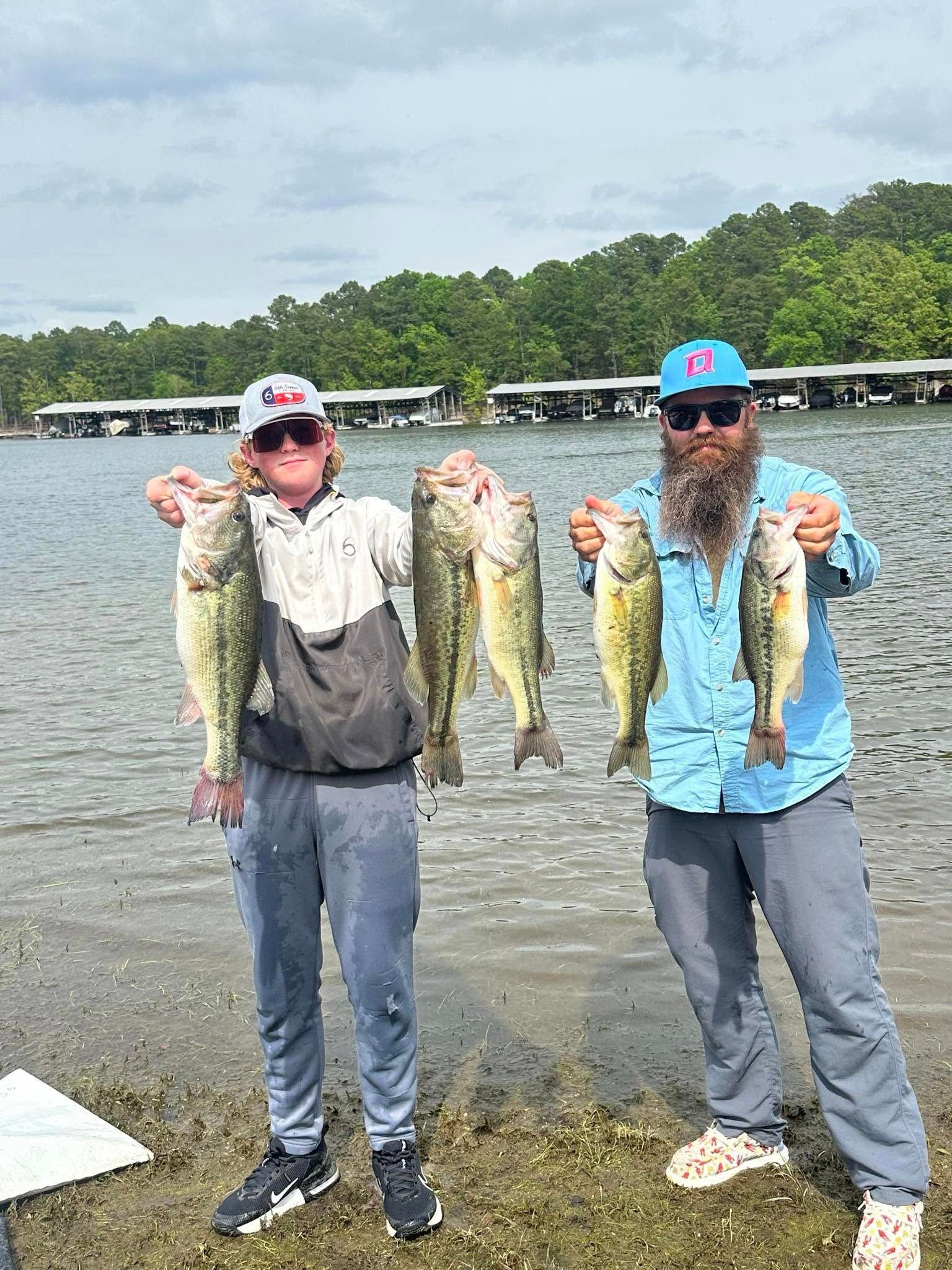 Two anglers holding up several large fish by a lakeshore on a cloudy day